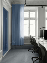 AVOLT office workspace with rows of desks, monitors and ergonomic chairs by tall windows and blue curtain