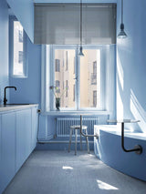AVOLT office kitchenette in soft blue with sink and black faucet, round table, metal stool and sunlit window.