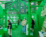 AVOLT pop-up interior in vibrant green, visitors browsing accessories and tote bags at display counters and interactive games