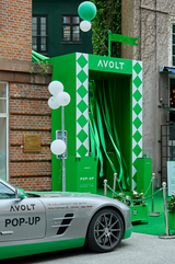 AVOLT green pop-up booth with ribbons, balloons and a branded silver sports car parked outside a brick building
