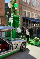 AVOLT street pop-up with green booth, balloons and visitors beside a silver sports car with open gullwing door.