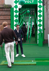 AVOLT event pop-up booth entrance with green decor, people playing mini-golf and branded balloons