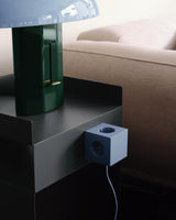 AVOLT power cube clipped to side table beside lamp and sofa, blue outlet cube with visible cable
